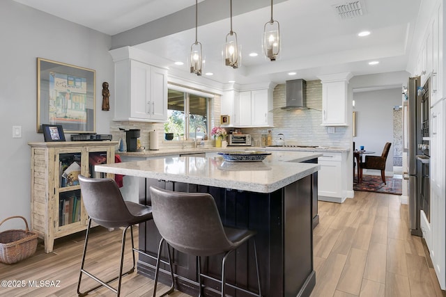 kitchen featuring a center island, wall chimney range hood, light stone countertops, light hardwood / wood-style floors, and white cabinets