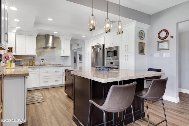 kitchen with white cabinetry, light stone counters, tasteful backsplash, appliances with stainless steel finishes, and wall chimney range hood