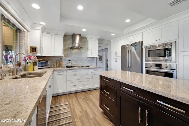 kitchen with sink, stainless steel appliances, light stone countertops, white cabinets, and wall chimney exhaust hood