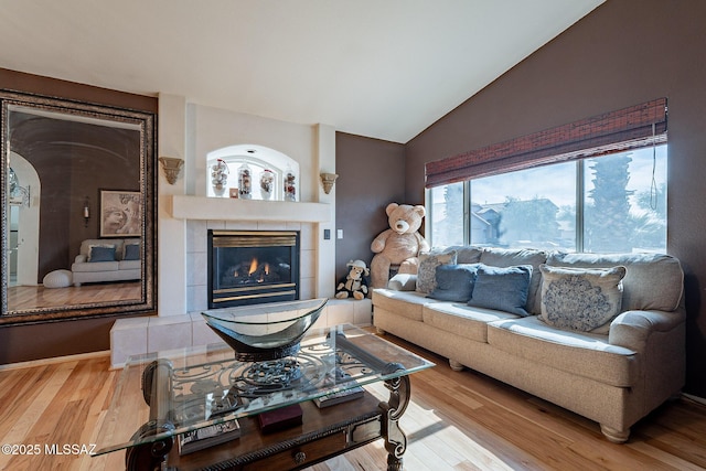 living area with vaulted ceiling, a tiled fireplace, and wood finished floors