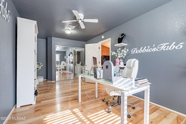 office space with light wood-type flooring, ceiling fan, visible vents, and a textured wall