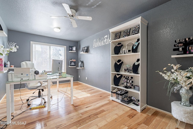 office space featuring ceiling fan, a textured ceiling, baseboards, and wood finished floors