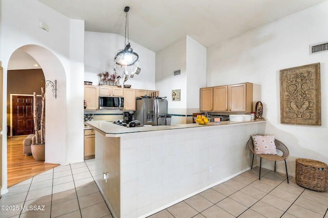 kitchen with hanging light fixtures, a peninsula, appliances with stainless steel finishes, and light brown cabinetry