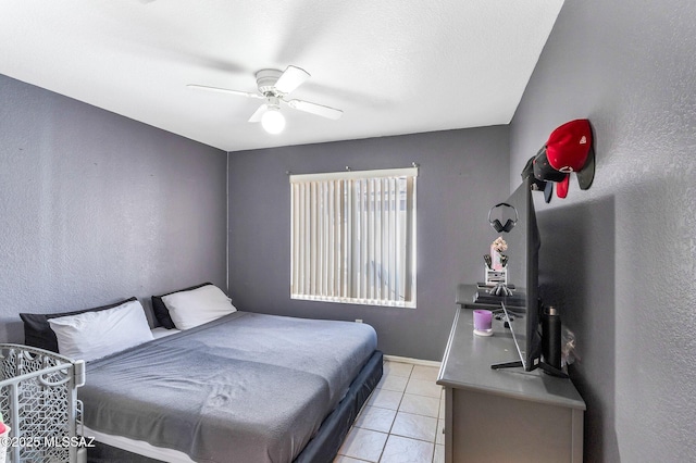 bedroom with a textured wall, ceiling fan, baseboards, and light tile patterned flooring