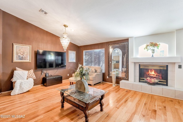 living area featuring a fireplace, visible vents, an inviting chandelier, vaulted ceiling, and hardwood / wood-style flooring