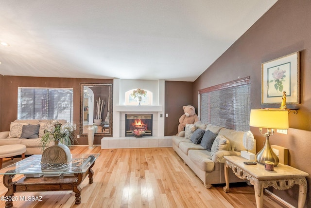 living room featuring a tiled fireplace, wood-type flooring, lofted ceiling, and plenty of natural light