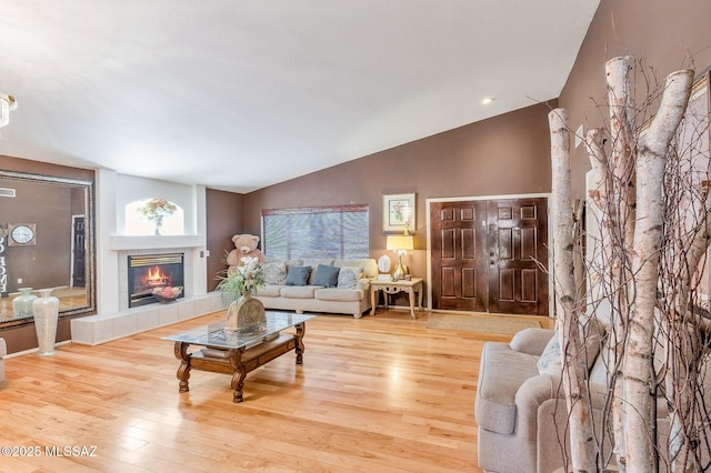 living room featuring lofted ceiling, light wood-style flooring, and a tile fireplace