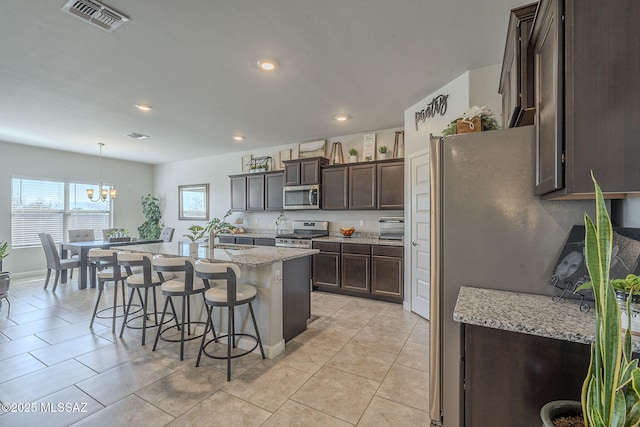 kitchen with a breakfast bar, light stone counters, hanging light fixtures, appliances with stainless steel finishes, and a kitchen island with sink