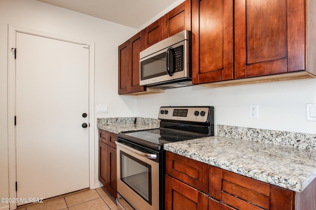 kitchen featuring appliances with stainless steel finishes, light tile patterned flooring, and light stone countertops