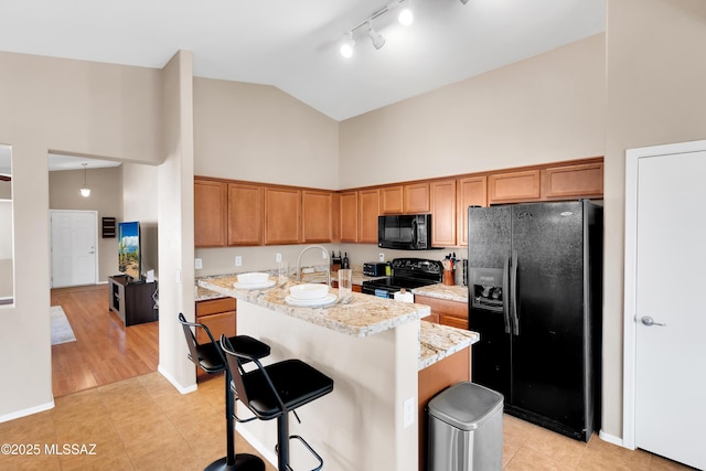 kitchen featuring high vaulted ceiling, a sink, black appliances, a kitchen bar, and a center island with sink