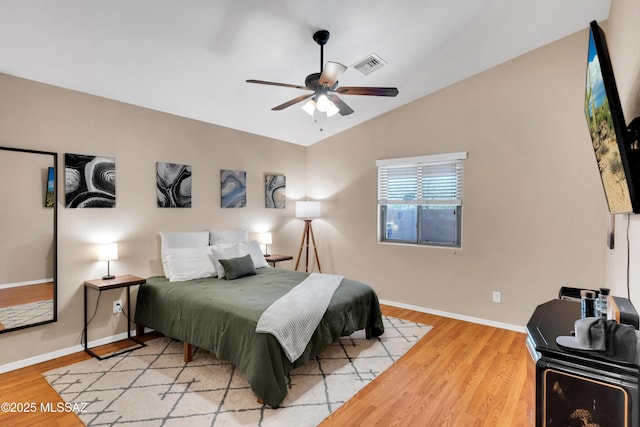 bedroom with vaulted ceiling, wood finished floors, visible vents, and baseboards