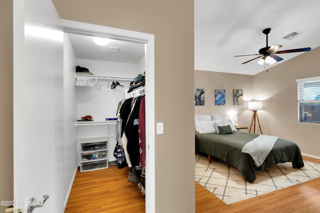 bedroom with ceiling fan, wood finished floors, visible vents, baseboards, and a closet