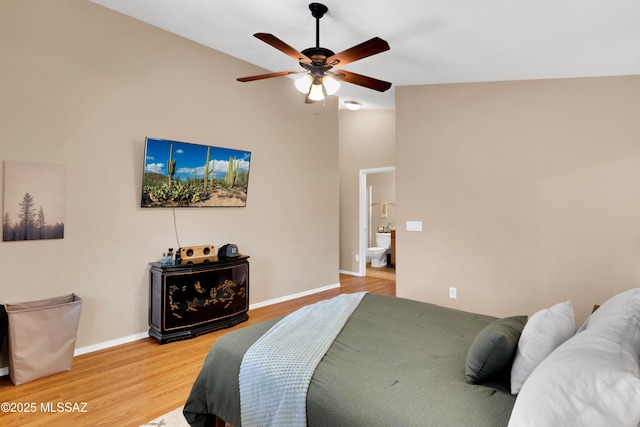 bedroom featuring baseboards, a ceiling fan, ensuite bath, light wood-style flooring, and vaulted ceiling