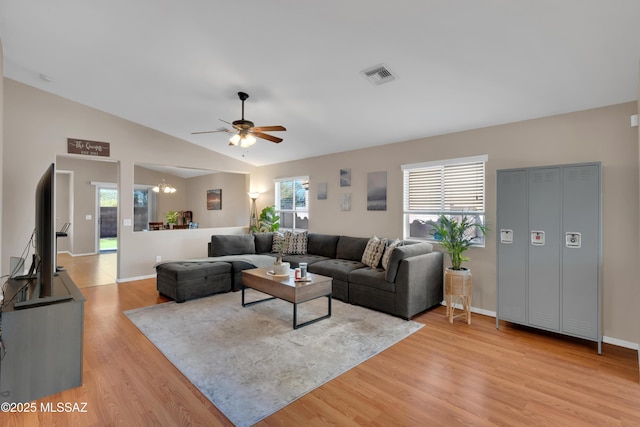 living area featuring lofted ceiling, visible vents, light wood-type flooring, baseboards, and ceiling fan with notable chandelier