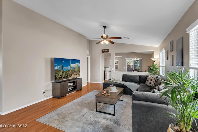 living area with visible vents, baseboards, lofted ceiling, wood finished floors, and ceiling fan with notable chandelier