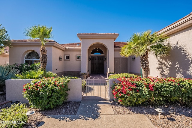 doorway to property with a gate, a tile roof, stucco siding, and fence