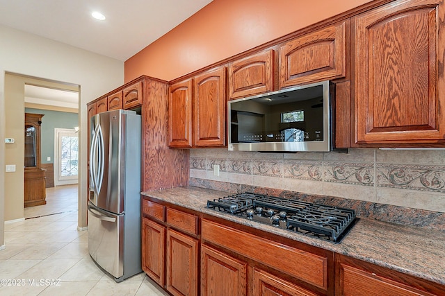 kitchen with light tile patterned flooring, appliances with stainless steel finishes, dark stone countertops, and decorative backsplash