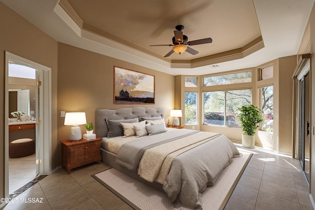 bedroom with light tile patterned floors, ensuite bath, a raised ceiling, and ceiling fan