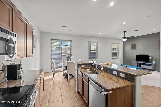 kitchen with stainless steel appliances, light tile patterned flooring, sink, and a center island with sink