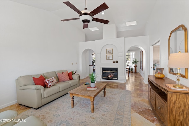 living area featuring arched walkways, high vaulted ceiling, ceiling fan, baseboards, and a glass covered fireplace