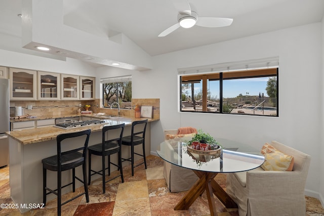 dining room with vaulted ceiling, stone finish flooring, a wealth of natural light, and a ceiling fan