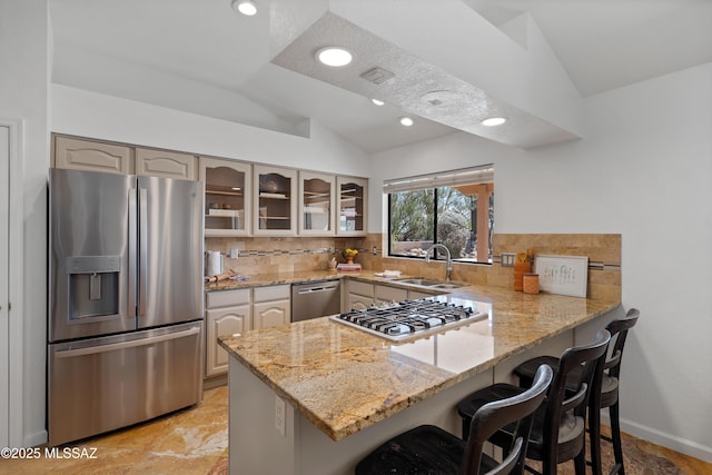 kitchen with glass insert cabinets, a peninsula, vaulted ceiling, stainless steel appliances, and a sink