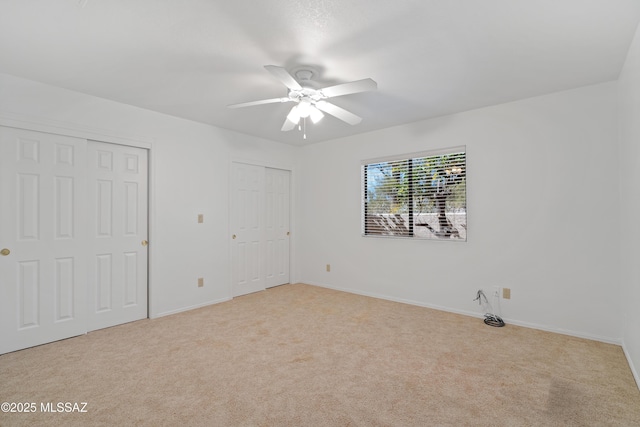 unfurnished bedroom with multiple closets, light colored carpet, ceiling fan, and baseboards