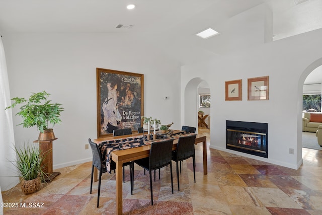 dining space featuring a glass covered fireplace, stone tile flooring, visible vents, and baseboards