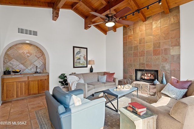 tiled living room featuring a tile fireplace, track lighting, beamed ceiling, and wood ceiling