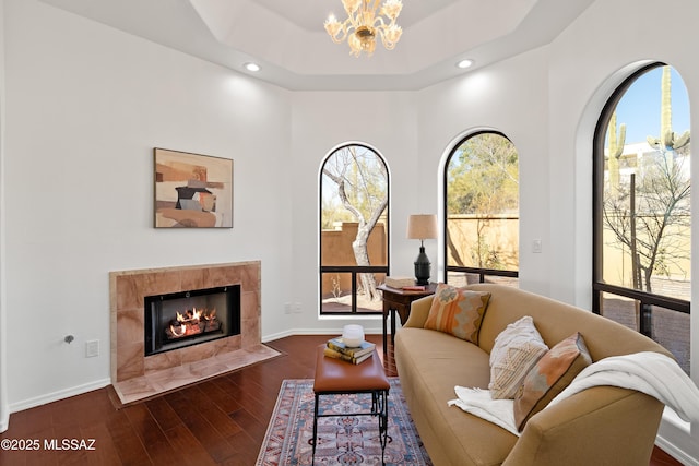 living room with dark hardwood / wood-style flooring, a tray ceiling, a fireplace, and a chandelier