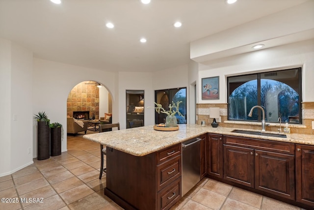 kitchen with dishwasher, sink, light stone counters, and kitchen peninsula