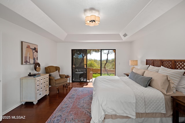 bedroom featuring a tray ceiling, dark hardwood / wood-style flooring, and access to outside