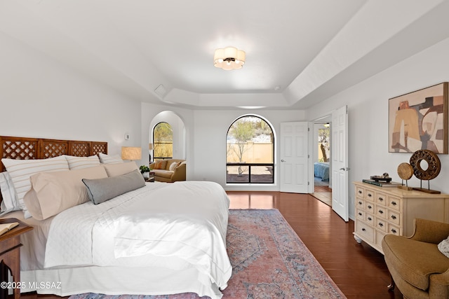 bedroom with a raised ceiling and dark hardwood / wood-style floors