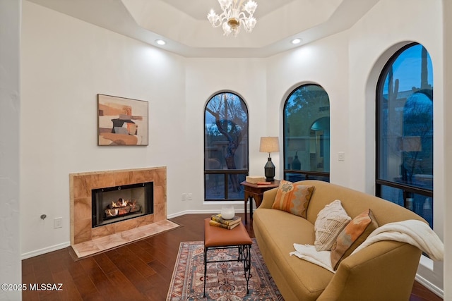 living room with a tray ceiling, an inviting chandelier, a high end fireplace, and dark hardwood / wood-style floors