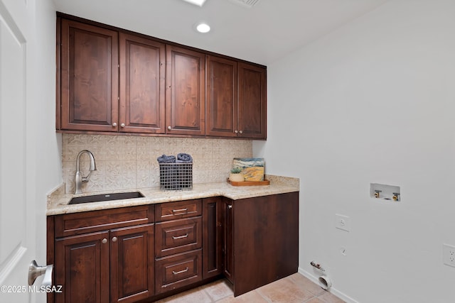 kitchen featuring tasteful backsplash, dark brown cabinetry, sink, and light stone counters