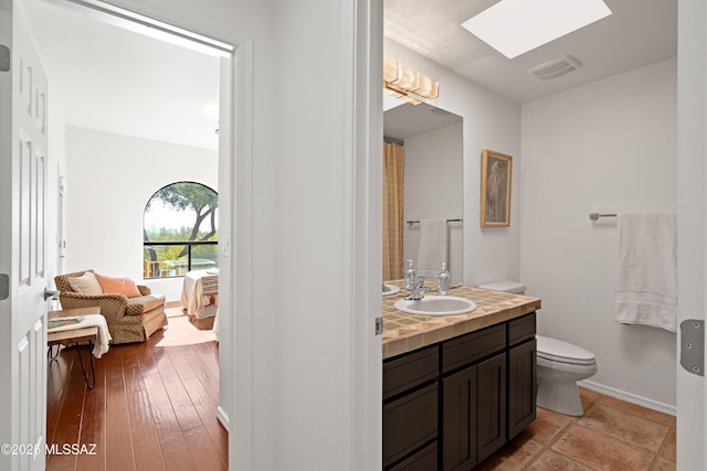 bathroom with toilet, a skylight, hardwood / wood-style floors, and vanity