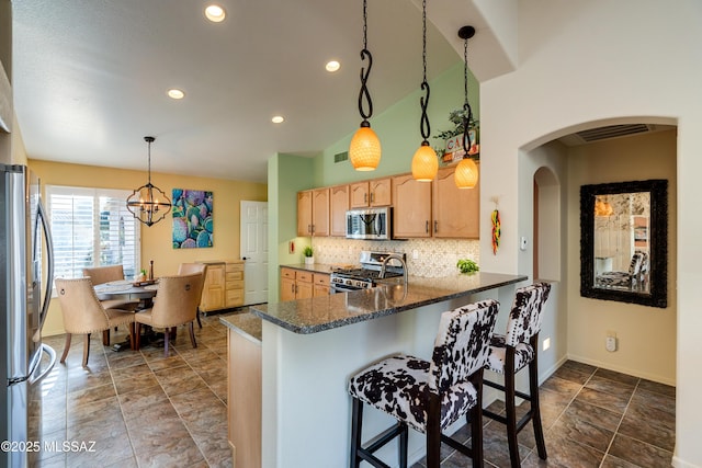 kitchen with hanging light fixtures, dark stone countertops, appliances with stainless steel finishes, kitchen peninsula, and backsplash