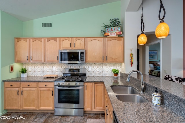 kitchen featuring sink, appliances with stainless steel finishes, hanging light fixtures, light brown cabinetry, and dark stone counters