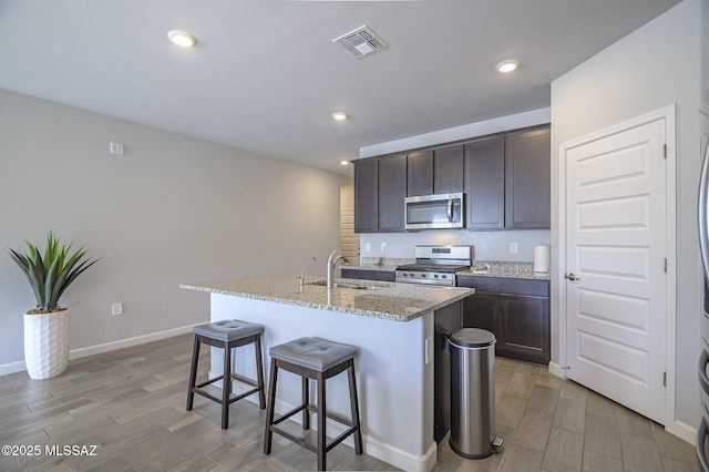 10139 N Sand Sage Trl, Marana, AZ 85653 - kitchen featuring sink, appliances with stainless steel finishes, dark brown cabinetry, light stone counters, and an island with sink