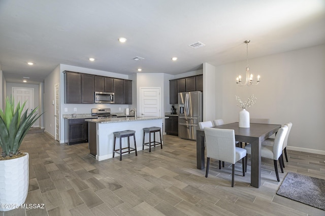 10139 N Sand Sage Trl, Marana, AZ 85653 - kitchen with appliances with stainless steel finishes, decorative light fixtures, a kitchen island with sink, dark brown cabinets, and an inviting chandelier