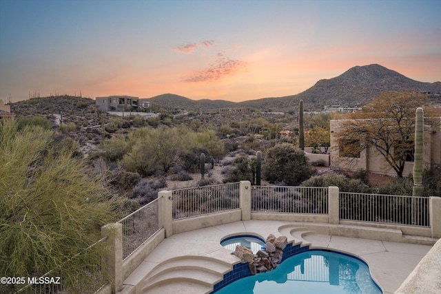 pool at dusk featuring a mountain view, a patio area, and an in ground hot tub