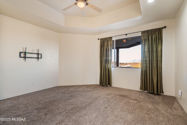 empty room with ceiling fan, a tray ceiling, and carpet floors