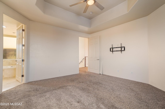 unfurnished room with a raised ceiling, light colored carpet, and ceiling fan