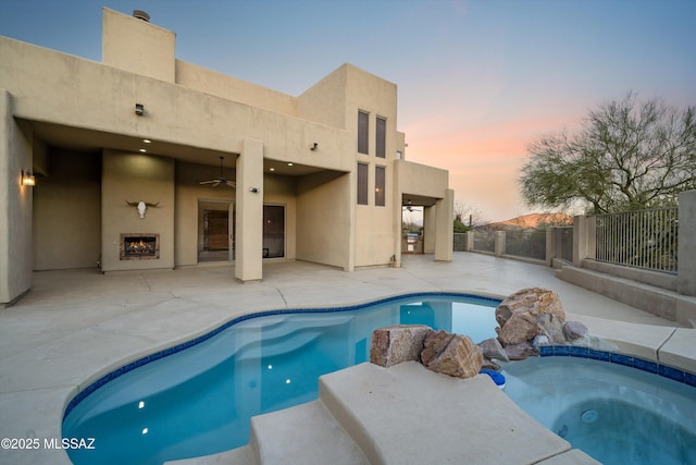 pool at dusk with ceiling fan, a patio area, and an outdoor fireplace