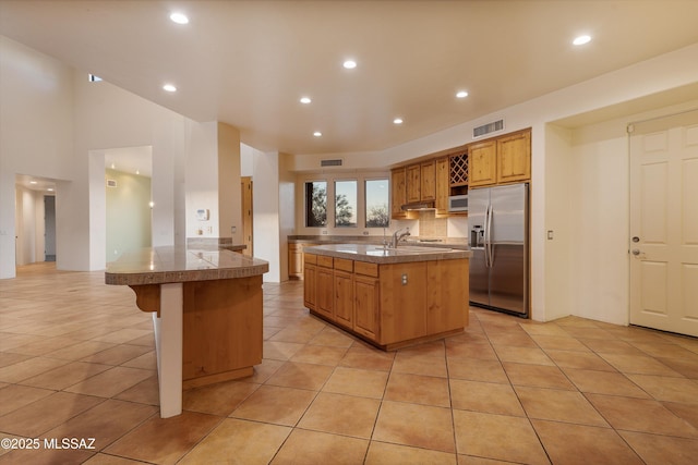 kitchen featuring stainless steel fridge with ice dispenser, a kitchen breakfast bar, light tile patterned floors, kitchen peninsula, and a center island with sink