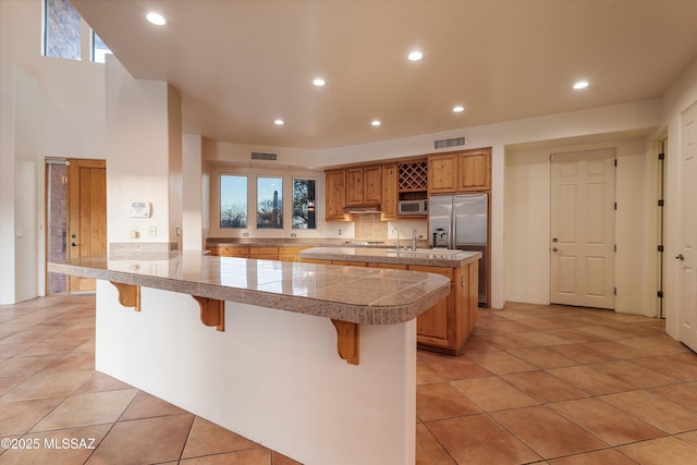 kitchen featuring light tile patterned floors, a kitchen breakfast bar, stainless steel appliances, tasteful backsplash, and kitchen peninsula