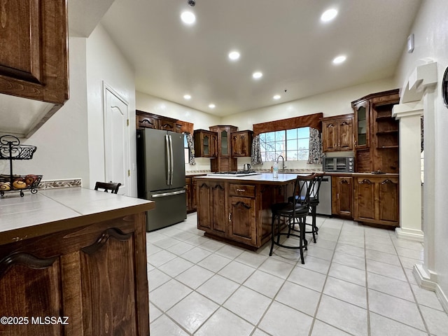 kitchen with a breakfast bar area, a center island, dark brown cabinets, light tile patterned floors, and stainless steel appliances