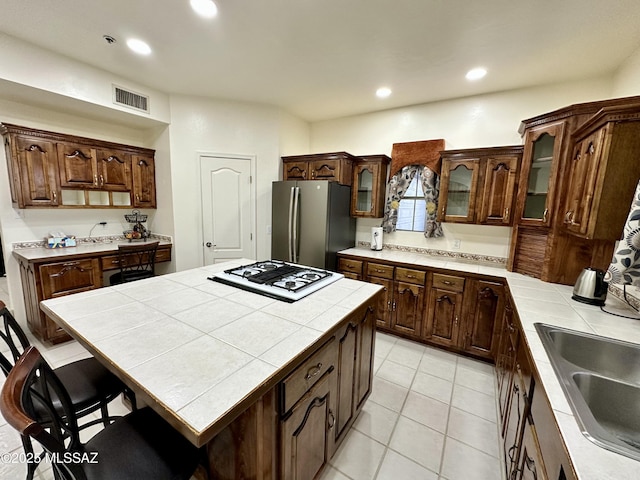 kitchen with stainless steel refrigerator, a center island, tile counters, white gas stovetop, and light tile patterned flooring