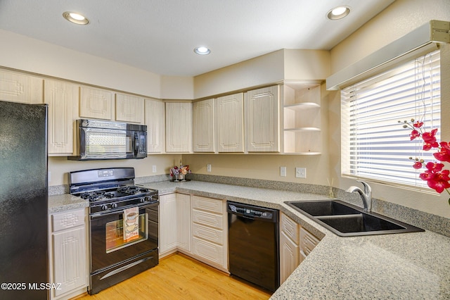 kitchen with sink, light hardwood / wood-style flooring, black appliances, and light stone countertops