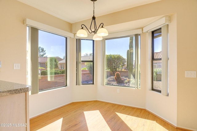 unfurnished dining area featuring an inviting chandelier, a healthy amount of sunlight, and light wood-type flooring